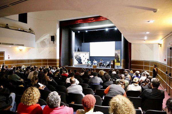 #PraCegoVer: Foto do fundo do auditório, durante o Seminário de Consciência Negra e entrega do Premio Edna Muniz. Público está sentado cadeiras e os palestrantes estão no palco. 